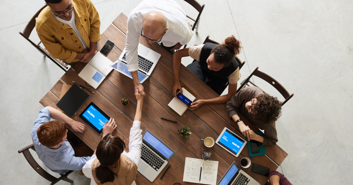 Nonprofit leadership team and cybersecurity advisor shaking hands at a conference table with laptops and tablets